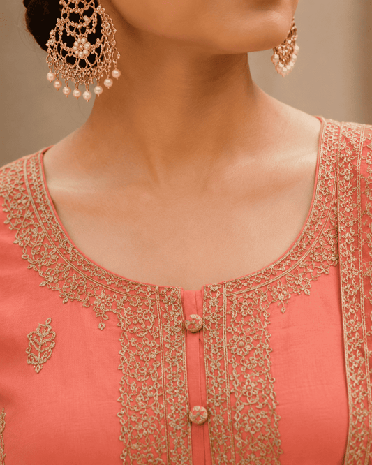 Semi-stitched peach cotton suit featuring delicate pastel thread and subtle sequin embroidery. The kurta is adorned with elegant motifs and a finely detailed hem border, paired with matching bottoms and a lightweight embroidered dupatta.