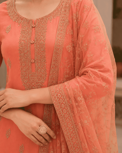 Semi-stitched peach cotton suit featuring delicate pastel thread and subtle sequin embroidery. The kurta is adorned with elegant motifs and a finely detailed hem border, paired with matching bottoms and a lightweight embroidered dupatta.